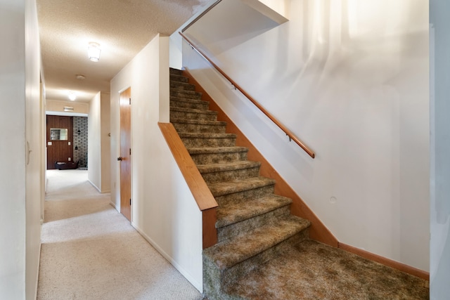 stairs featuring a textured ceiling and carpet flooring