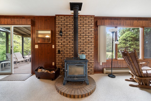 carpeted living room featuring baseboard heating, a wealth of natural light, a wood stove, and wooden walls