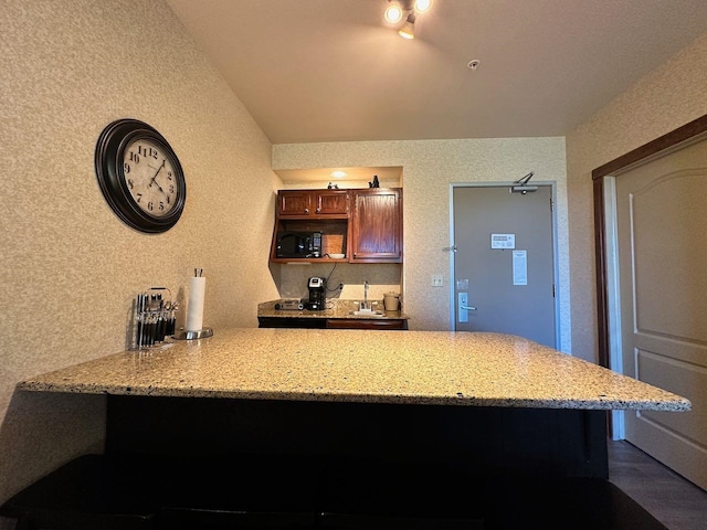 kitchen with kitchen peninsula, light stone counters, sink, and dark hardwood / wood-style floors