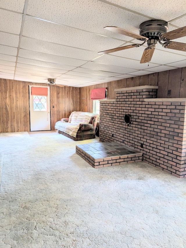 interior space with a drop ceiling, wood walls, carpet flooring, ceiling fan, and brick wall