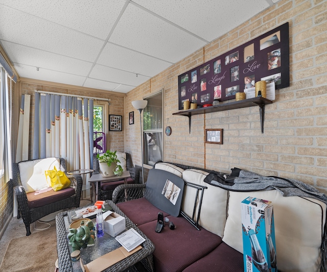 living room featuring a drop ceiling and brick wall