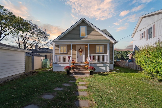 bungalow-style home with a lawn, a porch, and a storage shed