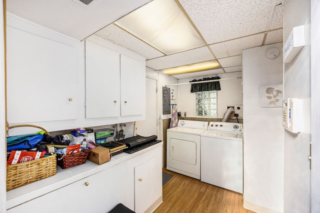 clothes washing area featuring separate washer and dryer, light hardwood / wood-style flooring, and cabinets