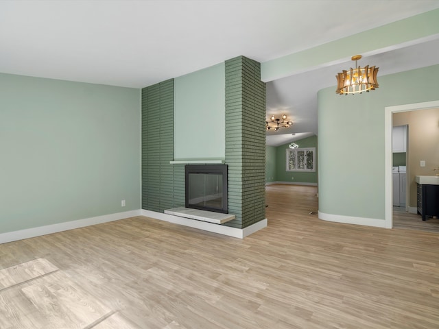 unfurnished living room featuring light hardwood / wood-style flooring, a notable chandelier, a fireplace, independent washer and dryer, and lofted ceiling