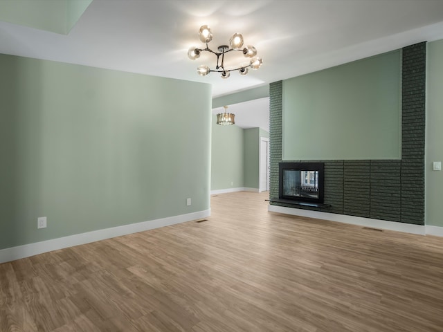 unfurnished living room featuring a large fireplace, a notable chandelier, and hardwood / wood-style flooring