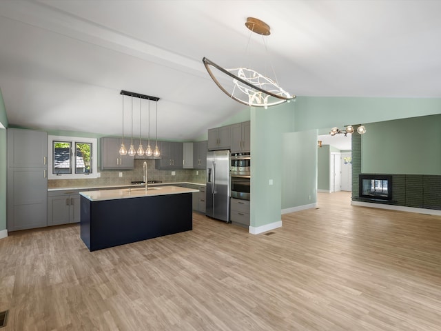 kitchen with gray cabinetry, lofted ceiling, light hardwood / wood-style flooring, an island with sink, and appliances with stainless steel finishes