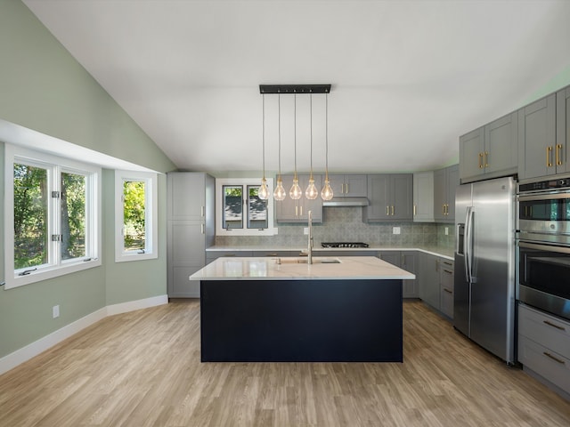 kitchen with light hardwood / wood-style floors, lofted ceiling, gray cabinets, a center island with sink, and appliances with stainless steel finishes