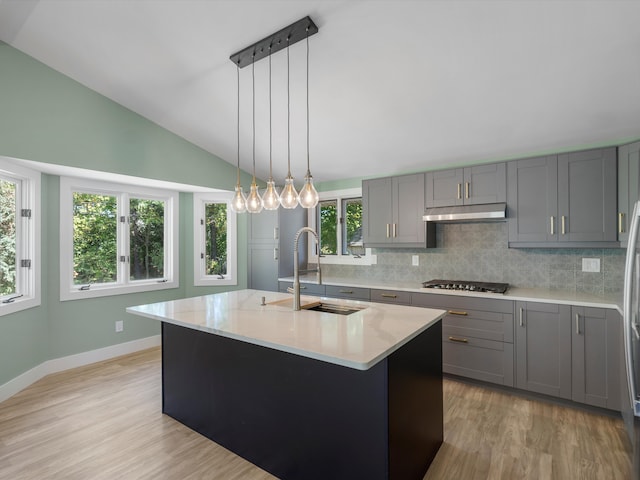 kitchen featuring a center island with sink, sink, vaulted ceiling, light wood-type flooring, and stainless steel gas cooktop