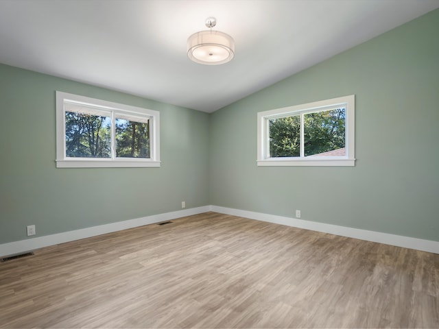 unfurnished room featuring lofted ceiling, light wood-type flooring, and a healthy amount of sunlight