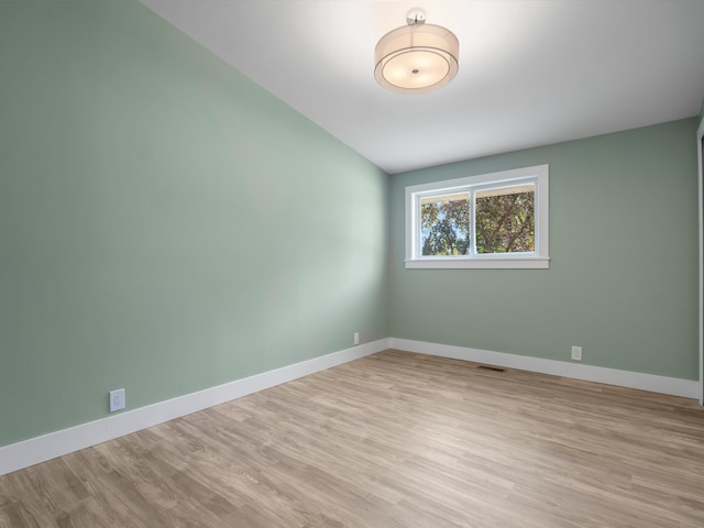 spare room featuring light wood-type flooring and vaulted ceiling