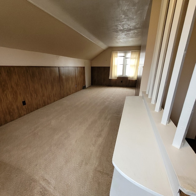 bonus room featuring a textured ceiling, light carpet, wood walls, and vaulted ceiling