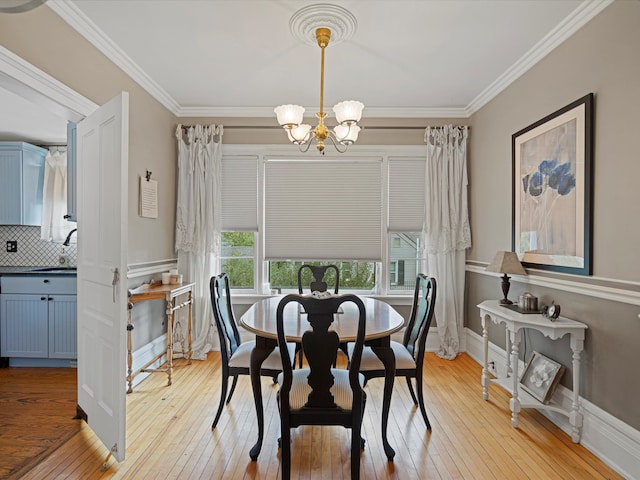 dining space featuring an inviting chandelier, ornamental molding, sink, and light hardwood / wood-style flooring