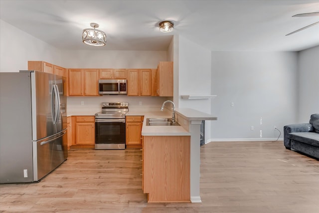 kitchen with kitchen peninsula, appliances with stainless steel finishes, light wood-type flooring, light brown cabinetry, and sink