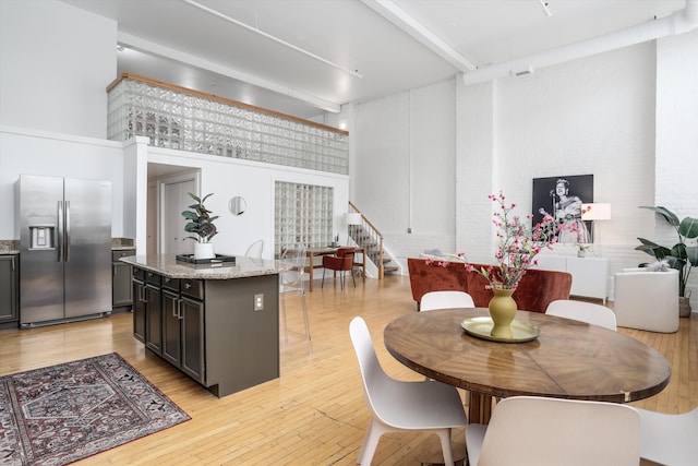 dining space with a towering ceiling, light hardwood / wood-style floors, and beamed ceiling