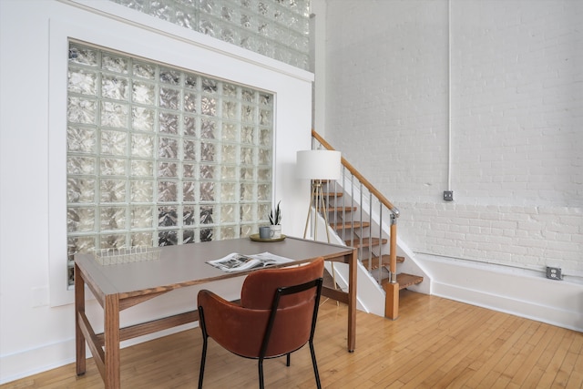 home office featuring a towering ceiling, brick wall, and hardwood / wood-style floors