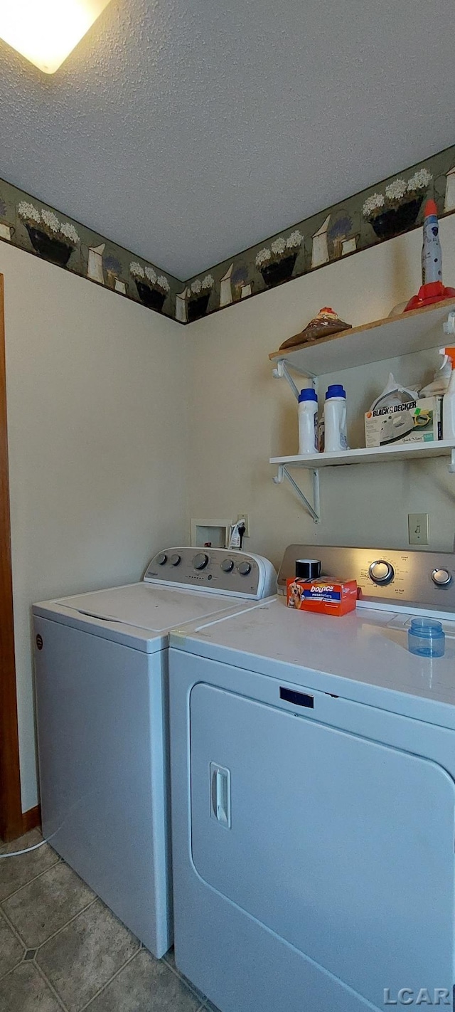 clothes washing area with light tile patterned floors, washer and dryer, and a textured ceiling