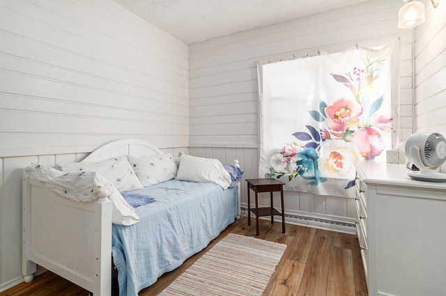 bedroom featuring a textured ceiling, wooden walls, and dark wood-type flooring