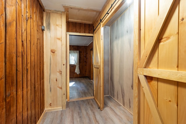 hall with light wood-type flooring, a barn door, and wood walls