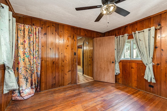 unfurnished room featuring wooden walls, ceiling fan, and hardwood / wood-style flooring