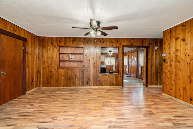 empty room with ceiling fan, light hardwood / wood-style floors, and wooden walls