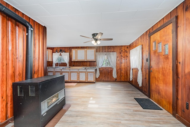 kitchen with a wood stove, wooden walls, ceiling fan, and light hardwood / wood-style floors