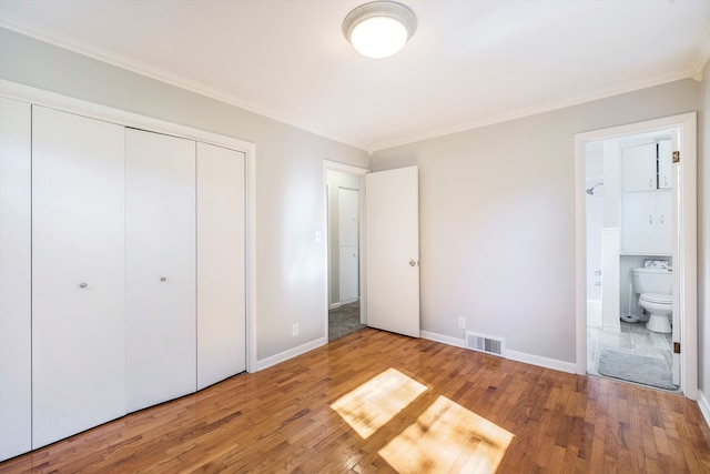 unfurnished bedroom featuring hardwood / wood-style floors, ensuite bathroom, crown molding, and a closet