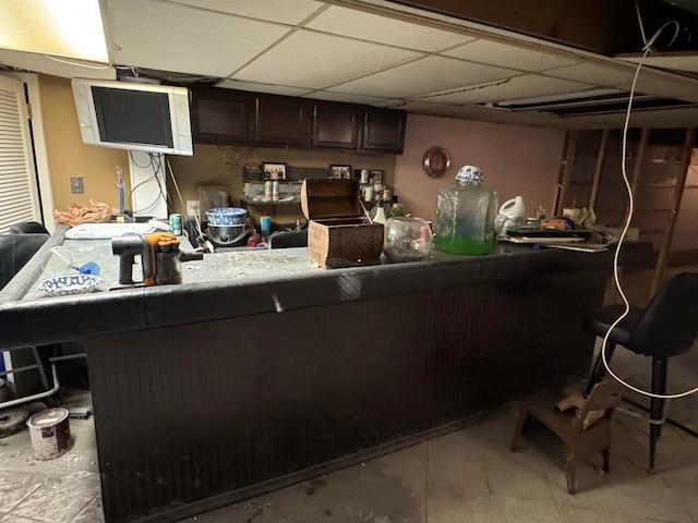 kitchen with kitchen peninsula, dark brown cabinetry, and a drop ceiling