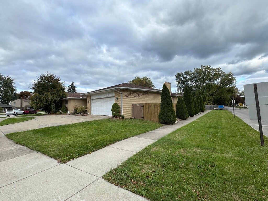 view of side of home with an attached garage, fence, a yard, and driveway