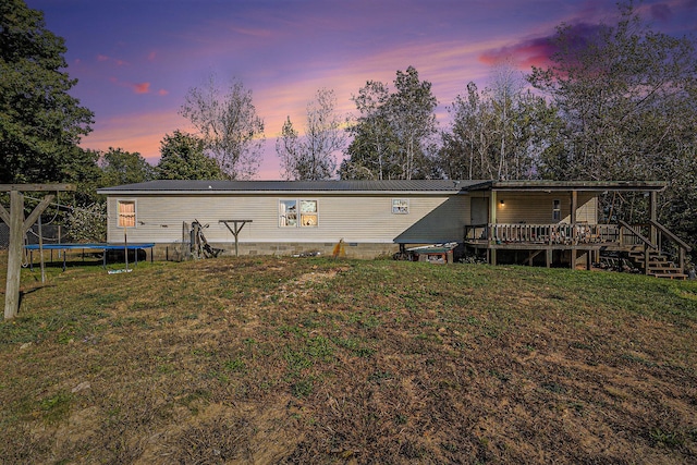 back house at dusk featuring a lawn, a deck, and a trampoline