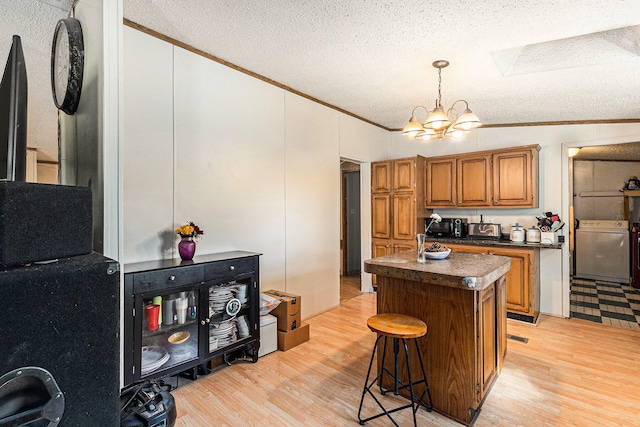 kitchen with lofted ceiling with skylight, a kitchen island, a textured ceiling, light hardwood / wood-style floors, and washer / dryer