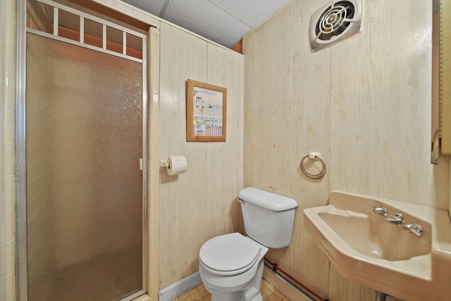 bathroom featuring sink, tile patterned floors, wood walls, toilet, and a shower with door