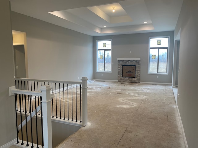 unfurnished living room with a tray ceiling and a stone fireplace