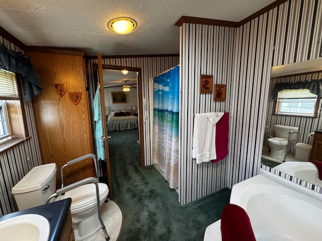 bathroom with a textured ceiling, ceiling fan, crown molding, toilet, and a bathing tub