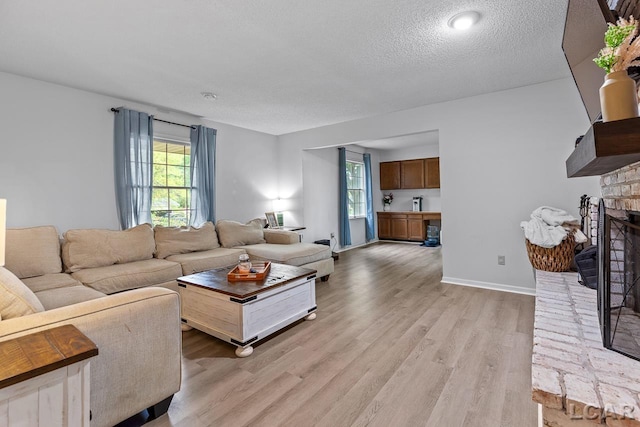 living room featuring light hardwood / wood-style flooring, a textured ceiling, and a brick fireplace