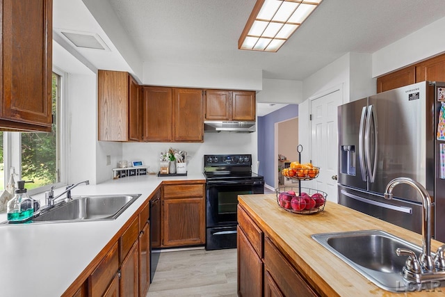 kitchen featuring butcher block countertops, light hardwood / wood-style flooring, black appliances, and sink