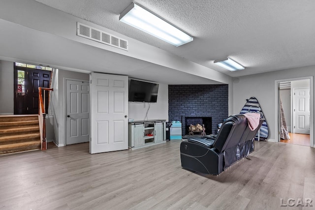 living room with a textured ceiling, hardwood / wood-style flooring, and a brick fireplace