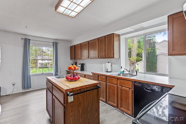 kitchen featuring dishwasher, sink, a kitchen island, a textured ceiling, and light hardwood / wood-style floors