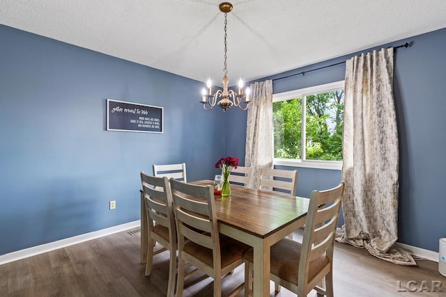 dining space featuring wood-type flooring, a textured ceiling, and a notable chandelier