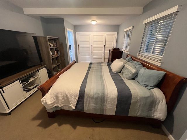 carpeted bedroom featuring beamed ceiling and a closet