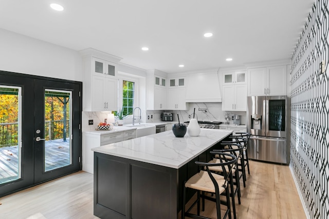 kitchen with stainless steel appliances, a kitchen island, light stone counters, white cabinets, and custom range hood