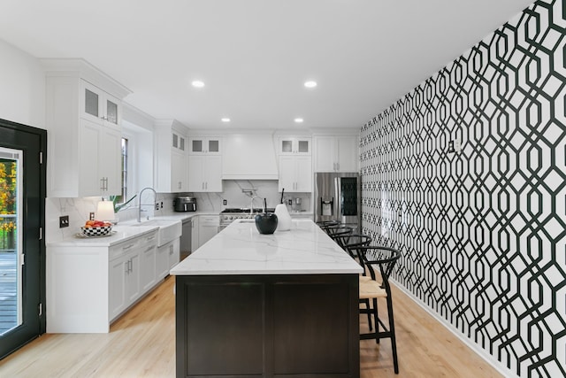 kitchen with sink, light hardwood / wood-style flooring, a kitchen island, white cabinetry, and stainless steel appliances