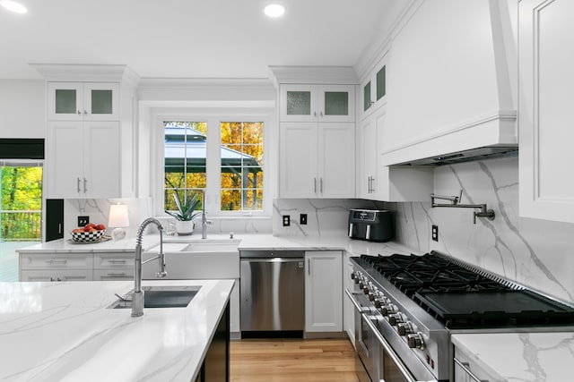 kitchen featuring light stone counters, premium range hood, decorative backsplash, white cabinets, and appliances with stainless steel finishes