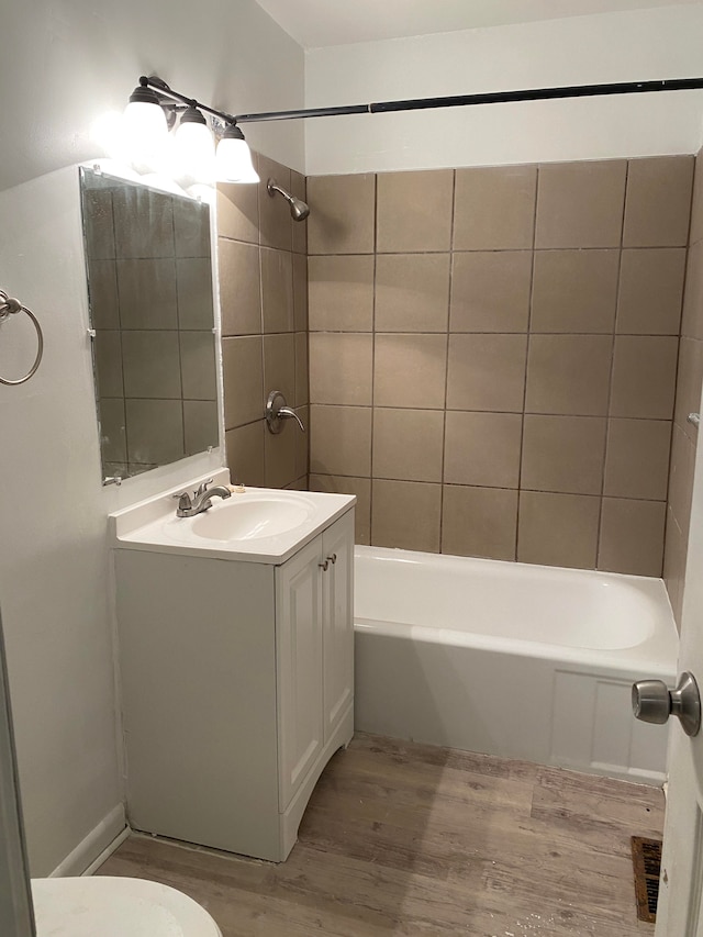 full bathroom featuring hardwood / wood-style flooring, tiled shower / bath combo, toilet, and vanity