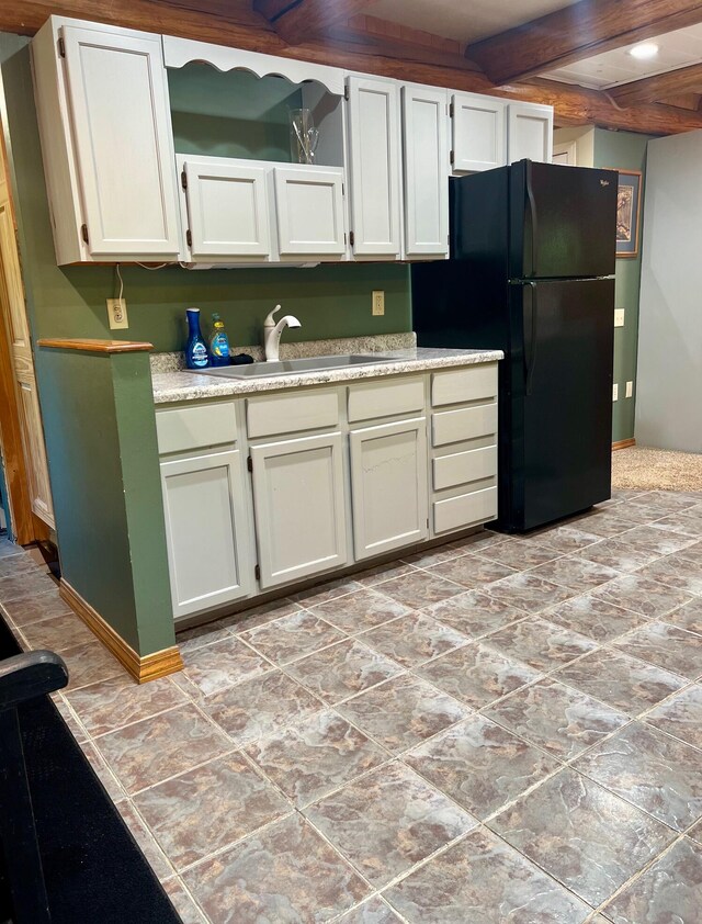 kitchen with beamed ceiling, black fridge, and sink