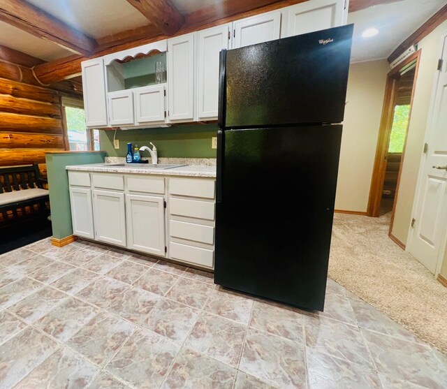 kitchen featuring white cabinetry, black fridge, sink, and beamed ceiling