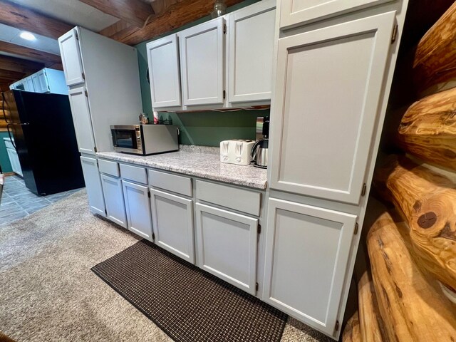 kitchen with beam ceiling, white cabinets, and light colored carpet