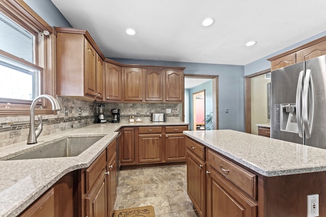 kitchen with backsplash, light stone countertops, sink, and stainless steel refrigerator with ice dispenser