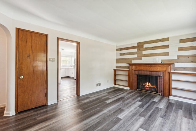 unfurnished living room with wood walls, dark hardwood / wood-style floors, and a brick fireplace