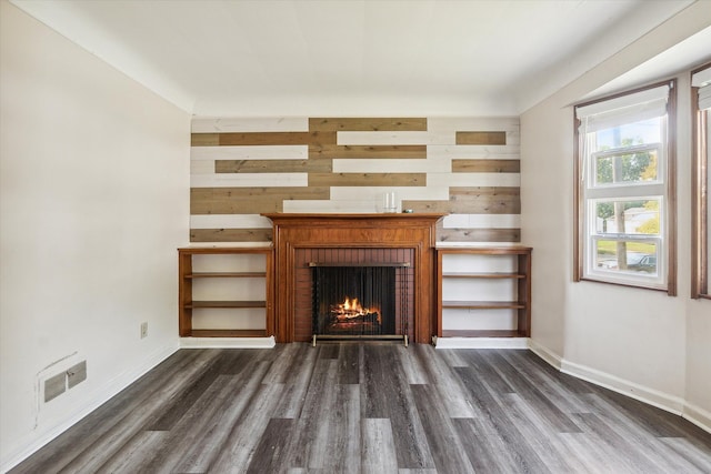 unfurnished living room with a fireplace, dark wood-type flooring, and wooden walls