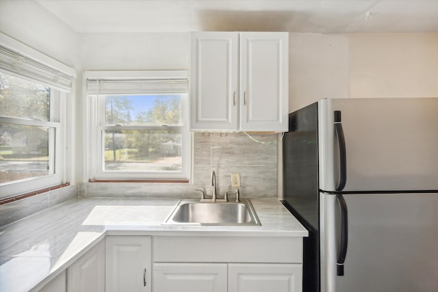 kitchen with stainless steel fridge, white cabinetry, sink, and tasteful backsplash